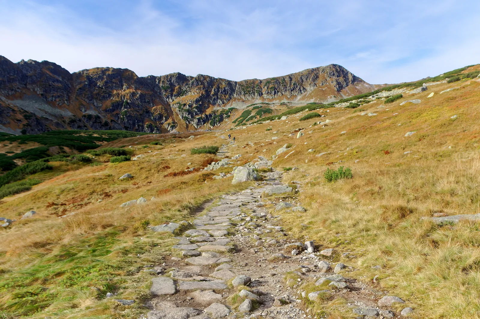 Die Dolina Pięciu Stawów Polskich im Tatra-Nationalpark im Oktober: ein Steinweg durch braunes Gras, dahinter Felsgrate