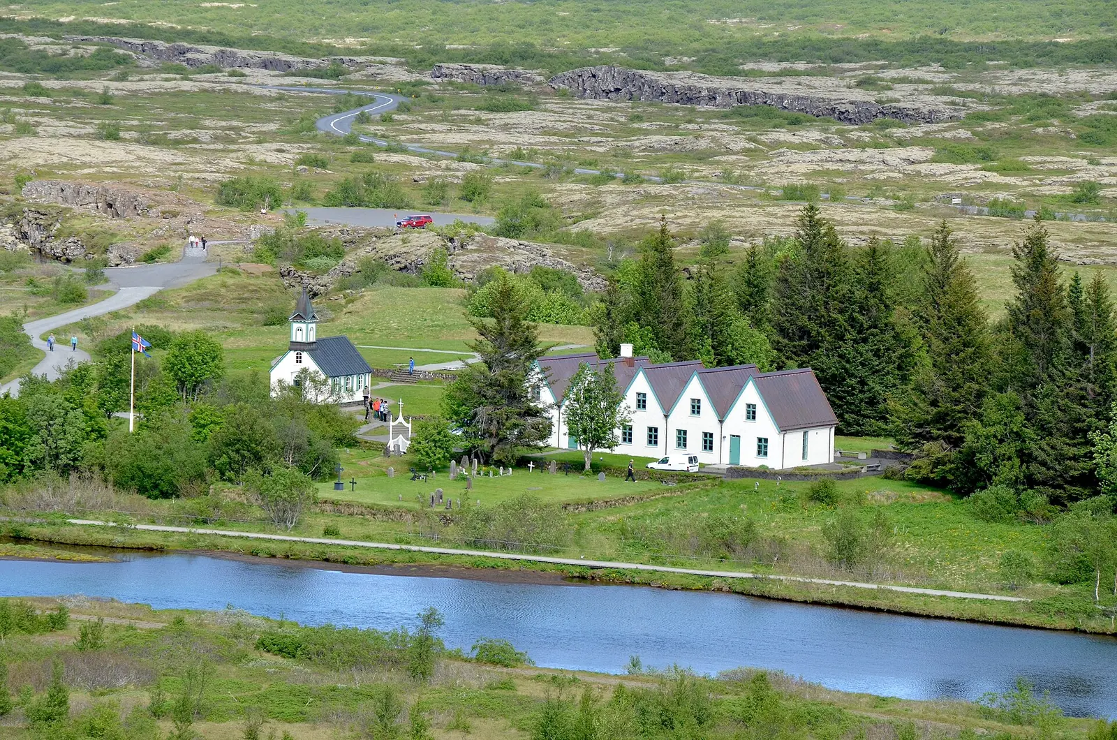 Die weiße Þingvallakirkja und die Giebel des Hofs Þingvallabær im Nationalpark Þingvellir, davor die Öxará, dahinter die Lavaebene