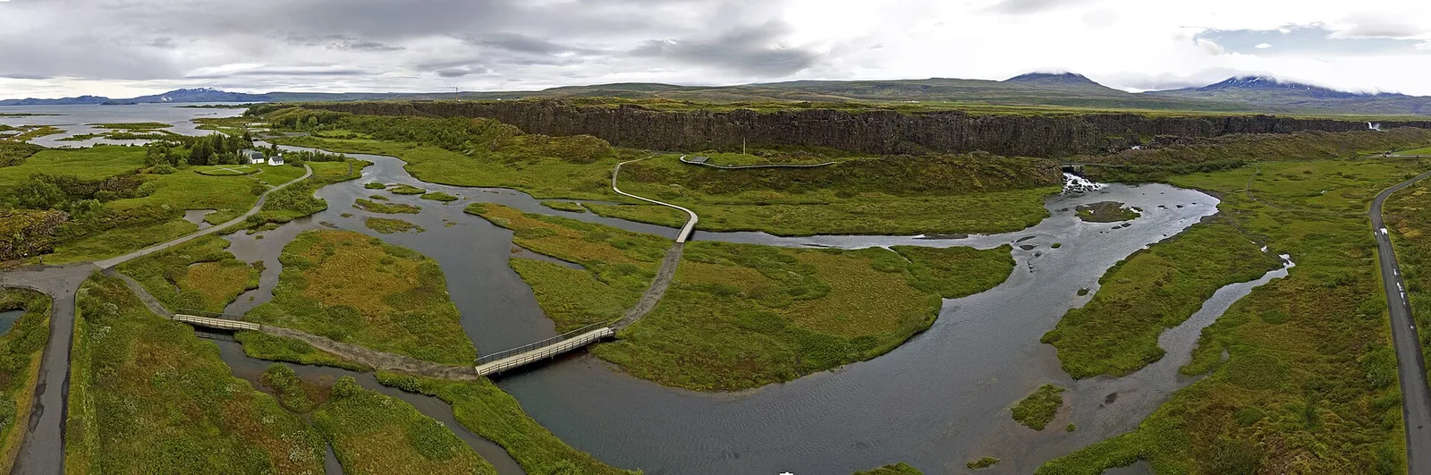 Luftbild über den Nationalpark Þingvellir: Wasserläufe der Öxará, Holzstege und Wege durch grüne Wiesen, am Horizont Berge
