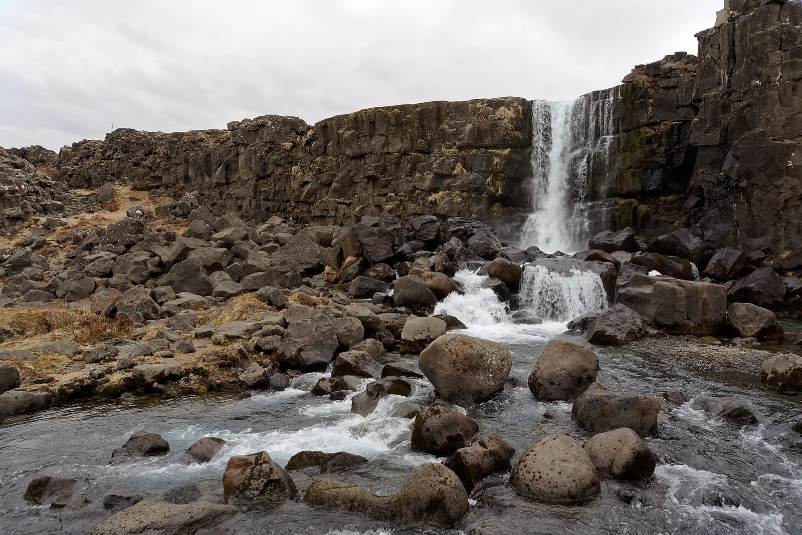 Der Öxarárfoss im Nationalpark Þingvellir stürzt über eine dunkle Basaltkante in ein Becken voller runder Felsblöcke