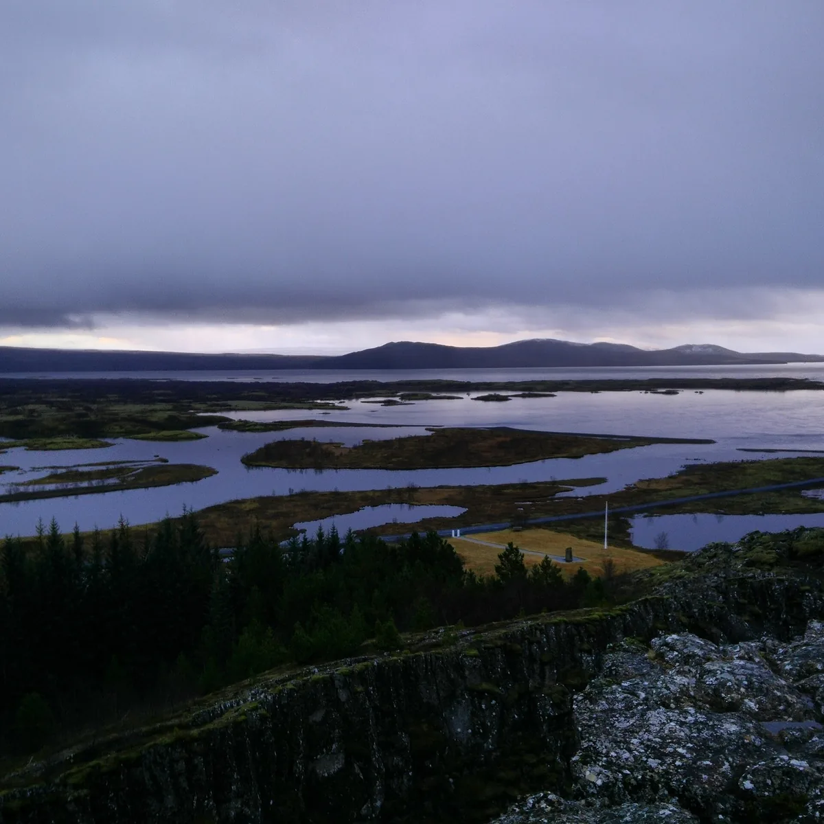 Blick über die Almannagjá auf den Þingvallavatn im Nationalpark Þingvellir unter tief hängenden Wolken