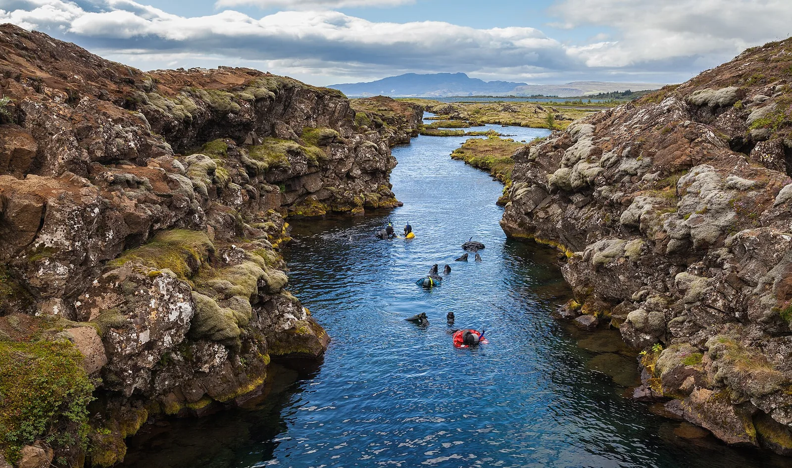 Schnorchler in Trockenanzügen treiben durch die Silfra-Spalte im Nationalpark Þingvellir zwischen bemoosten Lavawänden