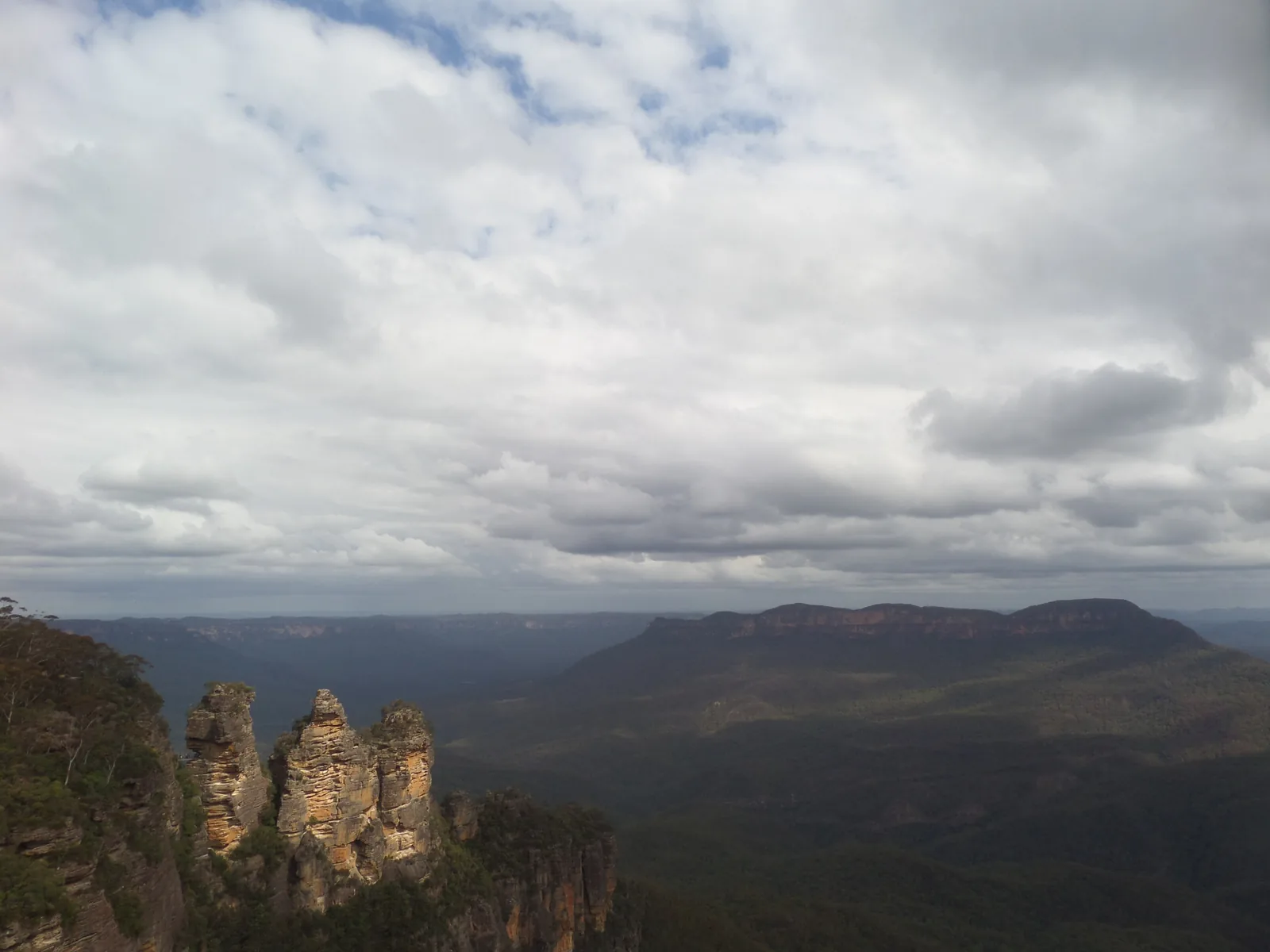 Die Three Sisters im Blue-Mountains-Nationalpark unter grauen Wolken, dahinter das Jamison Valley und der Tafelberg Mount Solitary