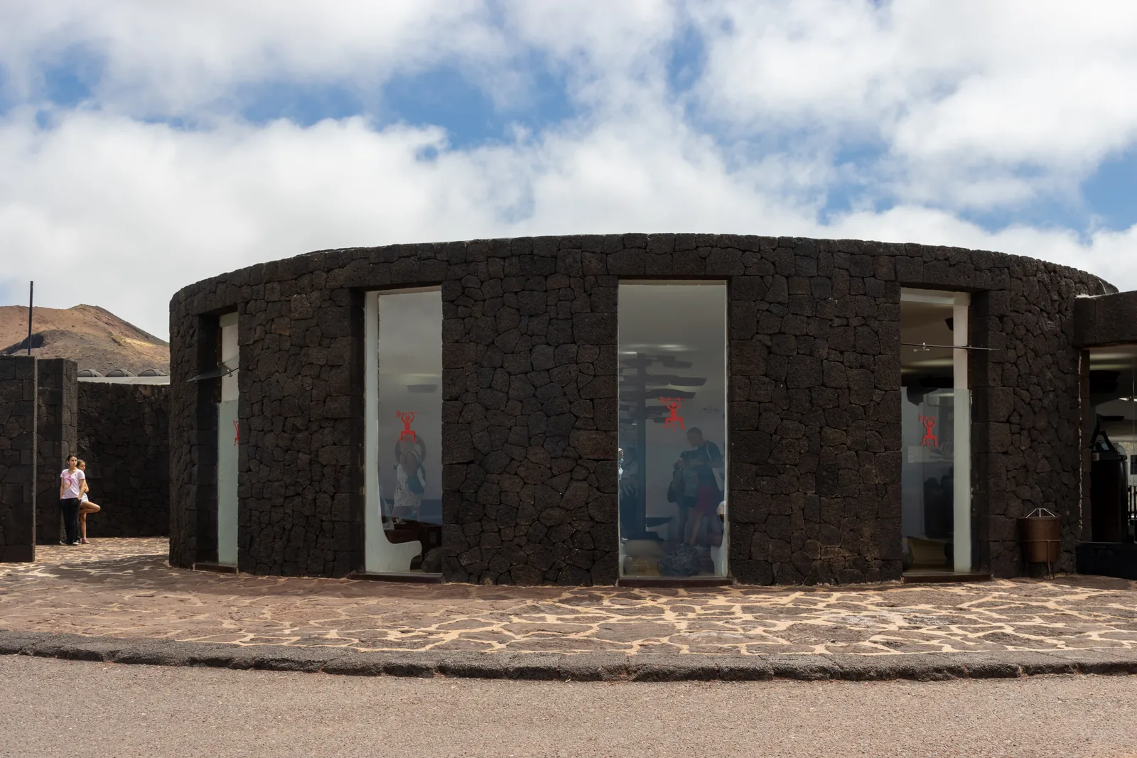 Das runde Gebäude aus schwarzem Lavastein auf dem Islote de Hilario mit Glasfront und Besuchern davor