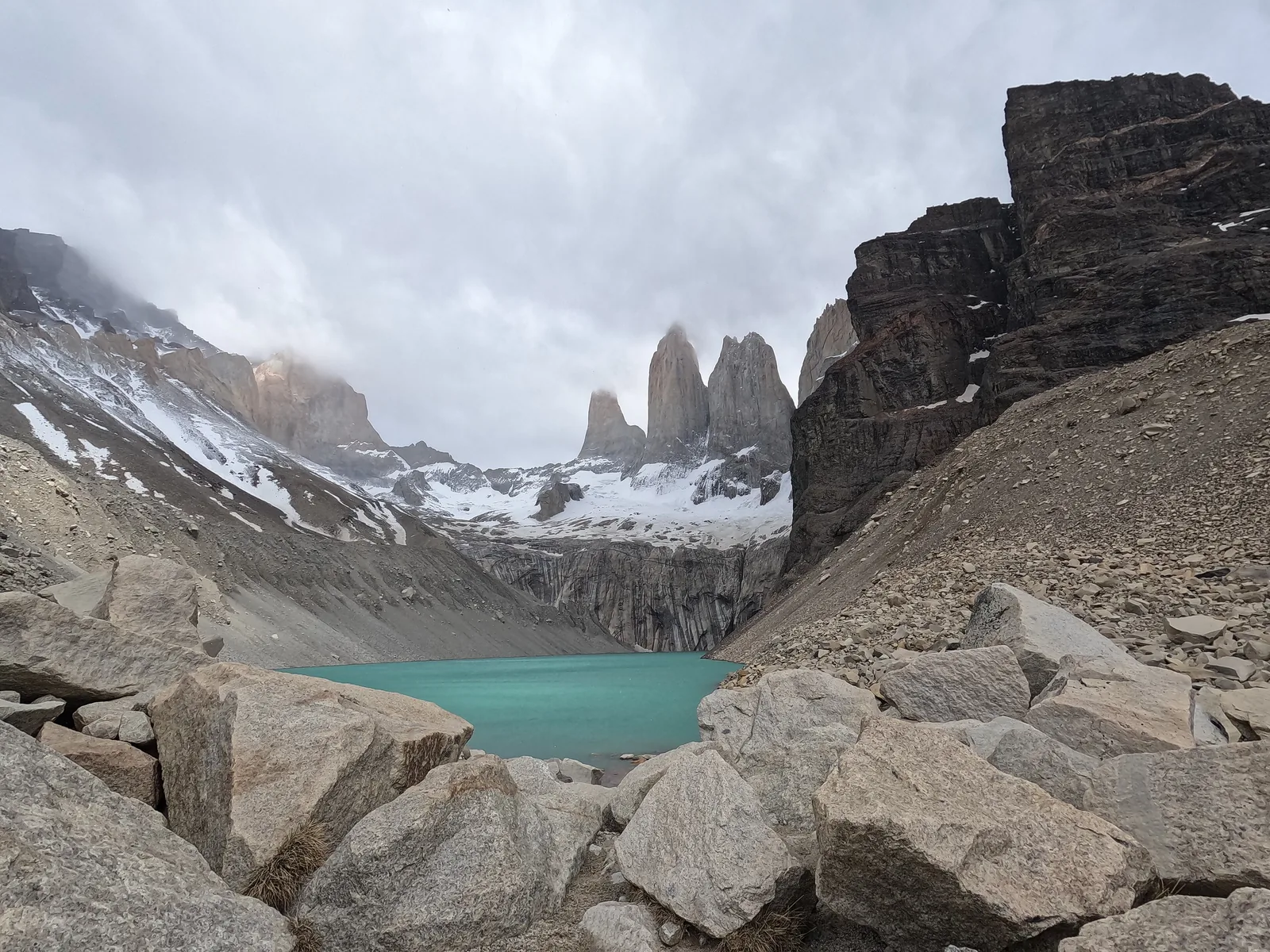 Der Mirador Base Torres im Nationalpark Torres del Paine: Felsblöcke einer Moräne, darunter der Gletschersee, dahinter die drei Granittürme