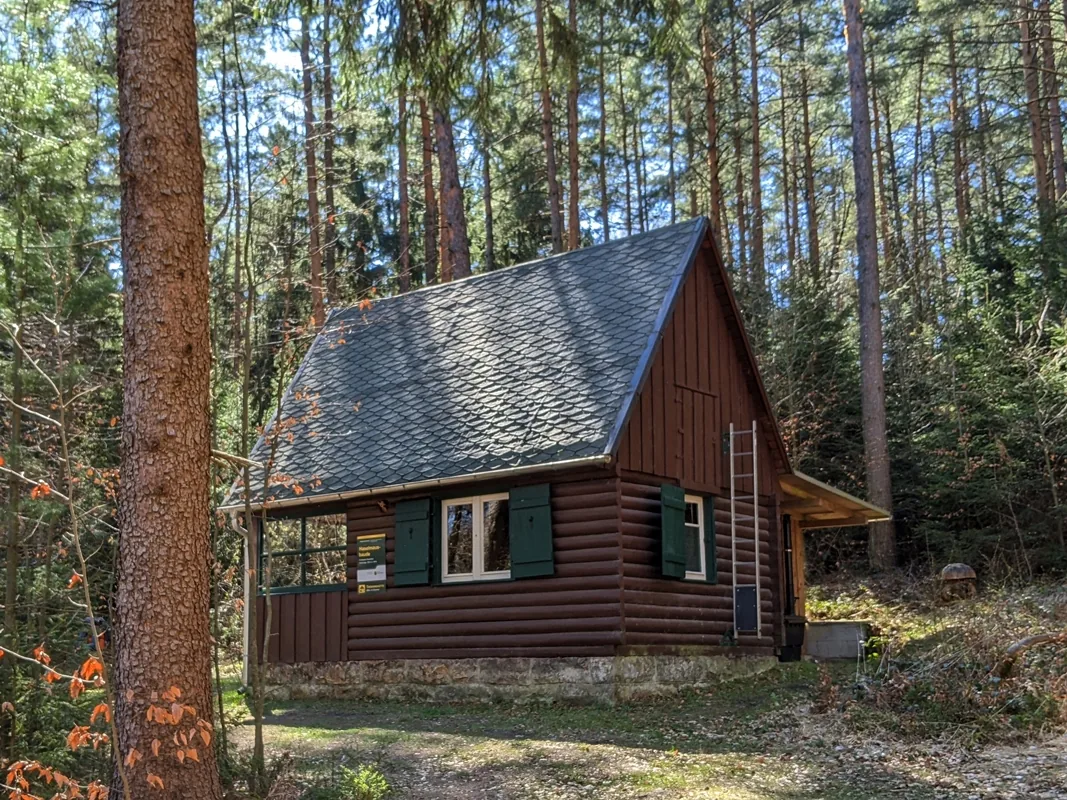 Trekkinghütte Haselmausbaude am Forststeig Elbsandstein, eine dunkle Holzhütte im Kiefernwald
