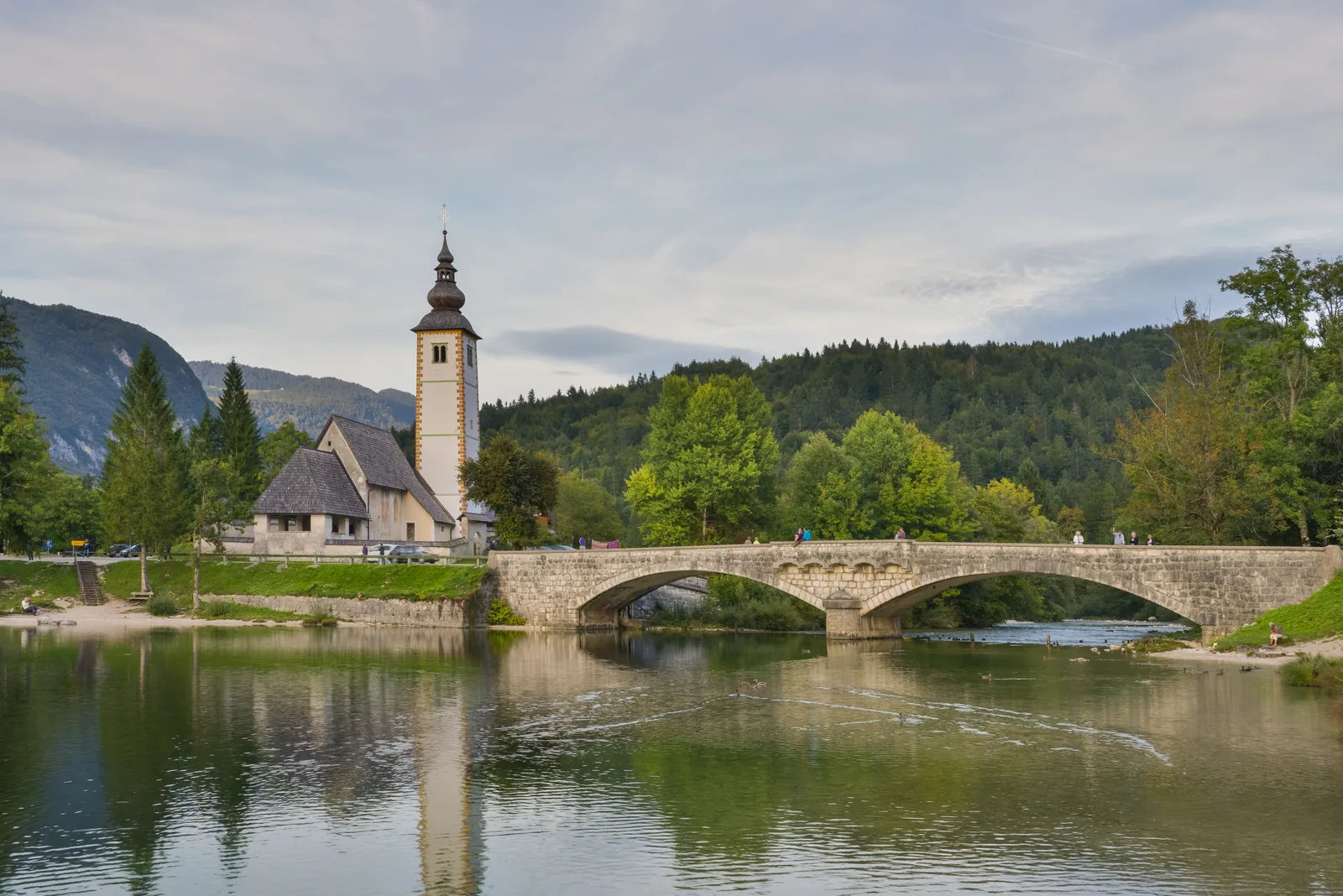 Die Kirche Johannes der Täufer und die Steinbrücke in Ribčev Laz am Ostufer des Bohinjer Sees