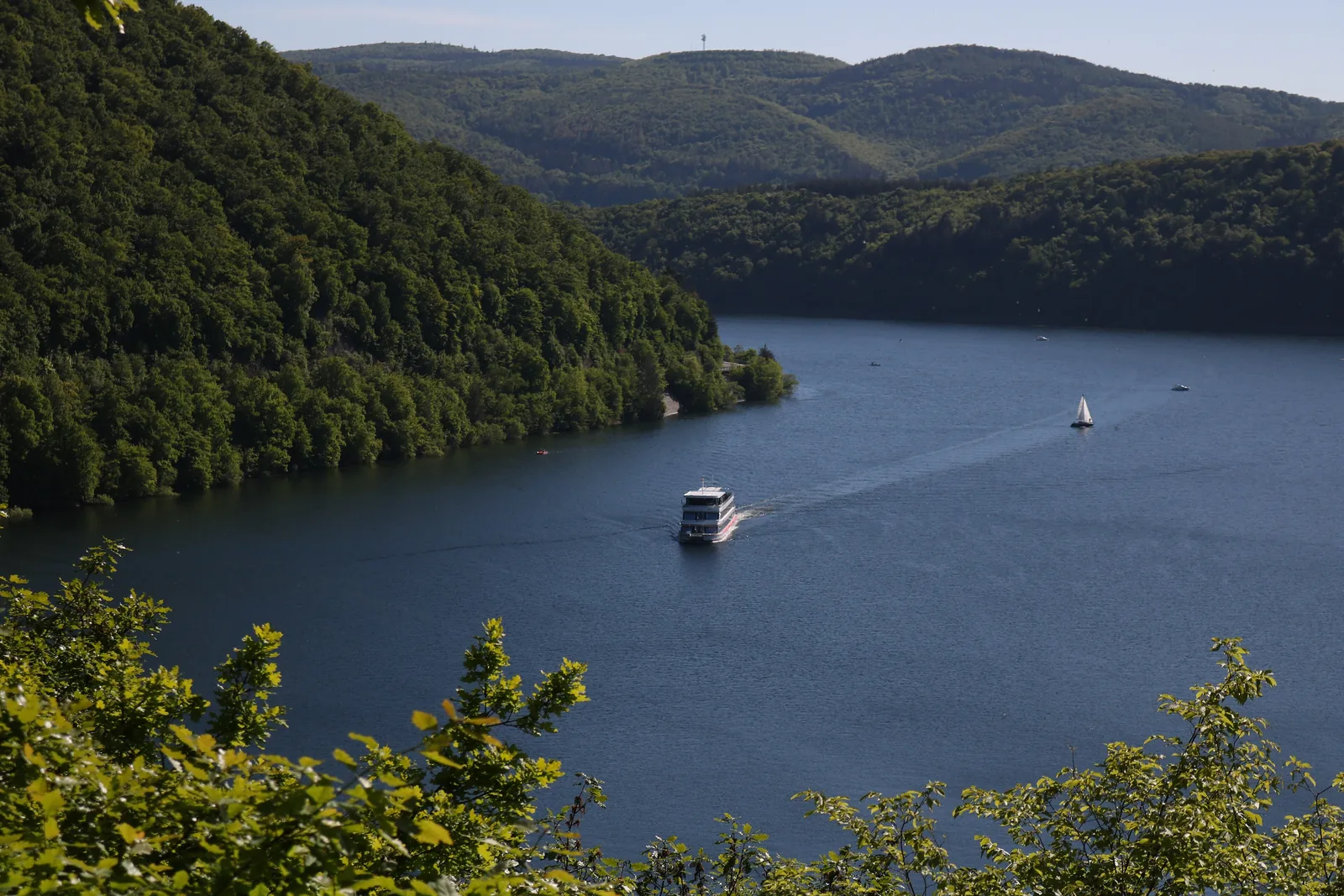 Blick vom Urwaldsteig Edersee auf den See mit Ausflugsschiff zwischen bewaldeten Hängen des Nationalparks Kellerwald-Edersee
