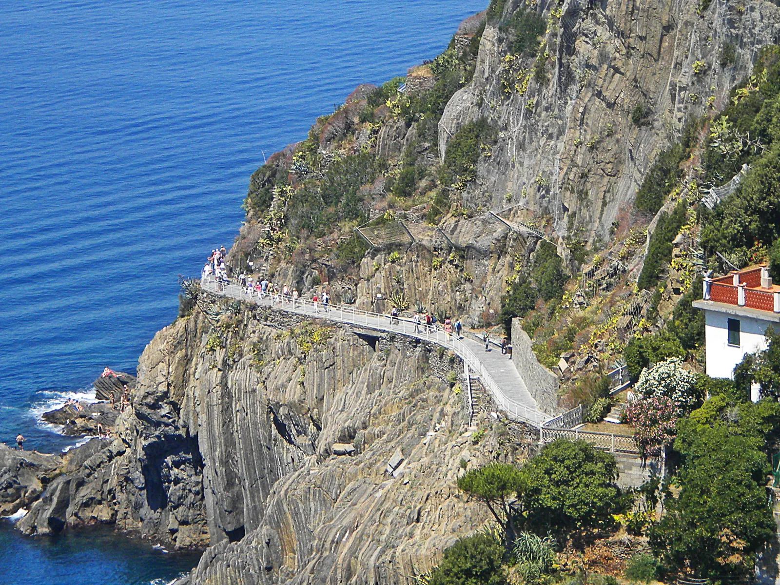 Die Via dell'Amore zwischen Riomaggiore und Manarola: ein heller Weg mit Geländer an der steilen Felsküste, darunter tiefblaues Meer