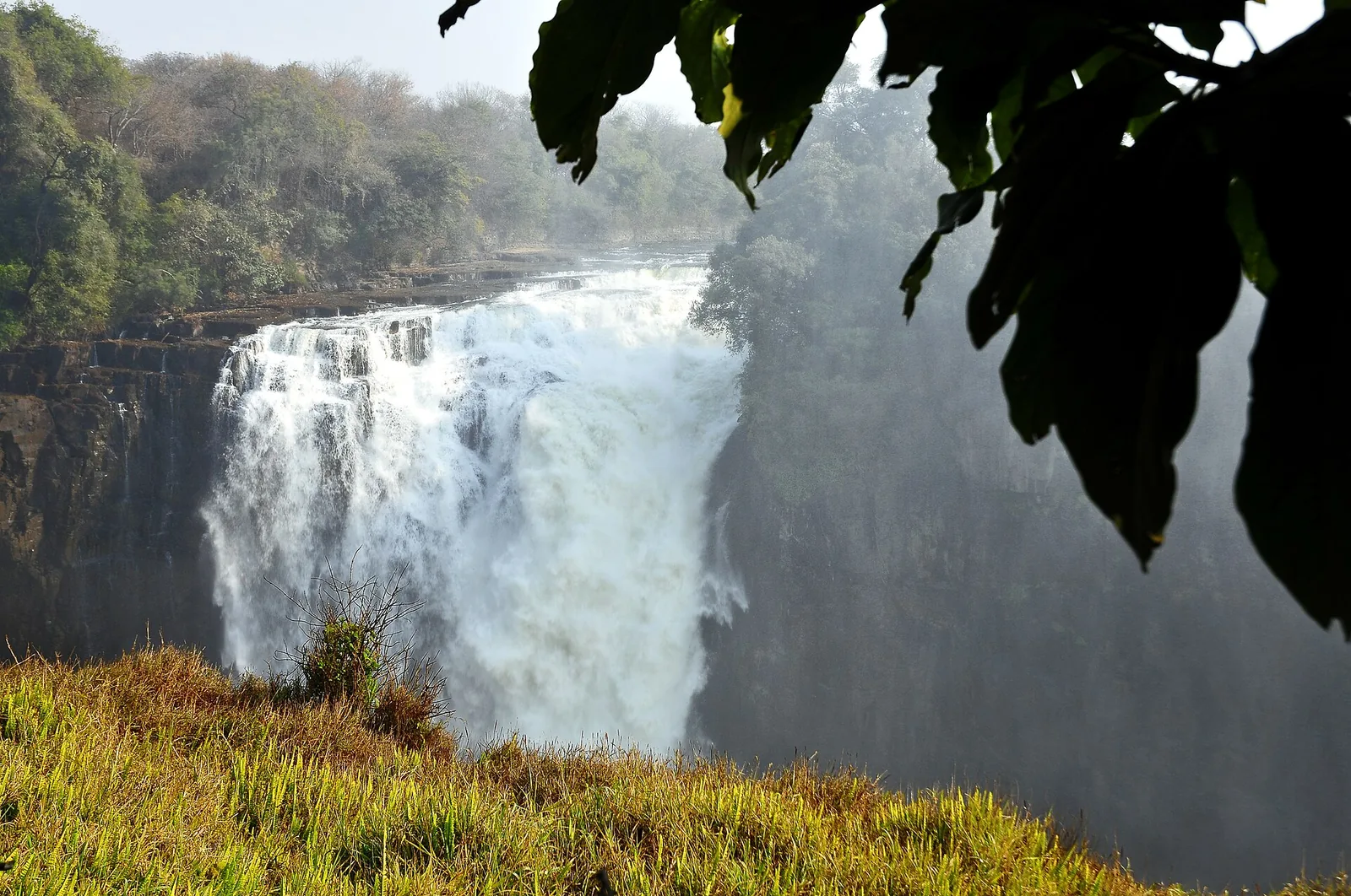 Wasser stürzt am Devil's Cataract der Victoria Falls zwischen grünen Felswänden in die Schlucht, Gischt steigt auf