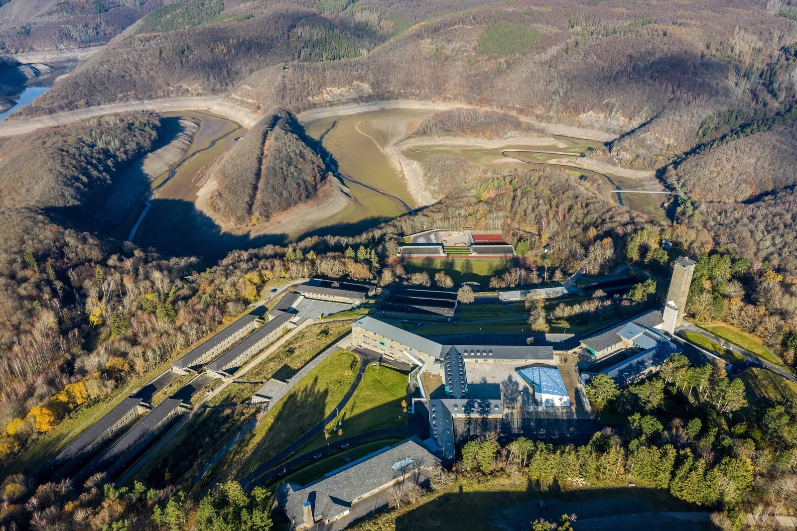 Luftbild von Vogelsang IP mit Turm, Forum und Kameradschaftshäusern über dem Tal des Urftsees, ringsum Wald des Nationalparks Eifel