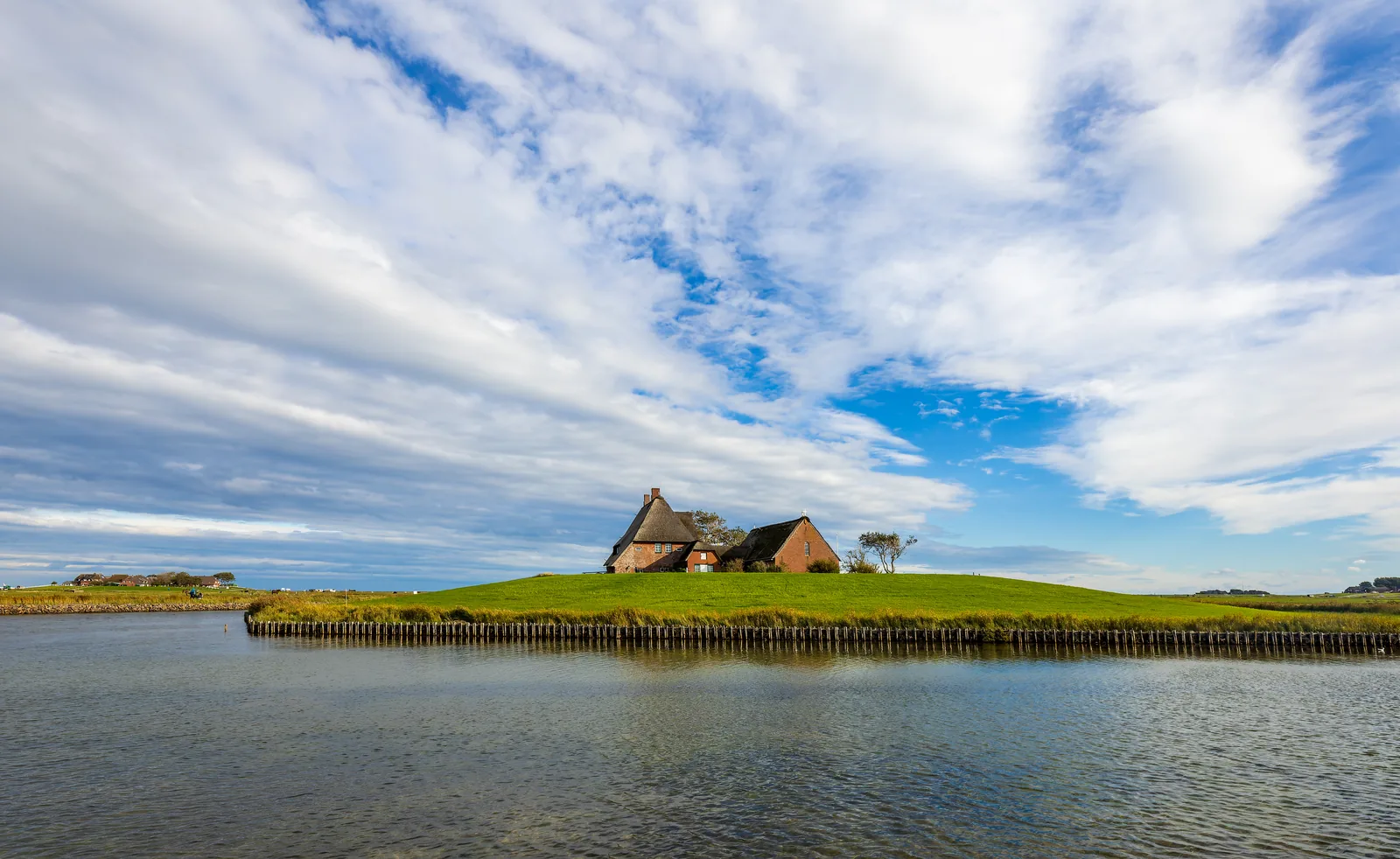 Die Kirchwarft auf Hallig Hooge: ein aufgeschütteter Hügel mit reetgedeckten Häusern, ringsum Wasser
