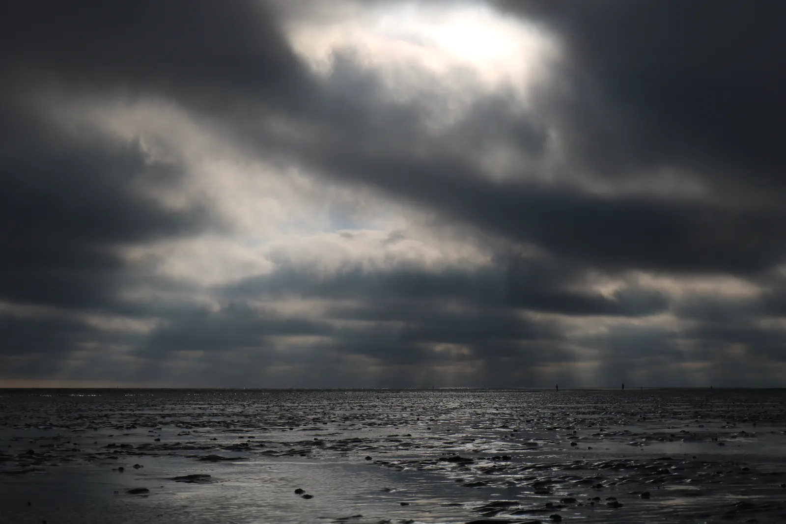 Dunkle Wolkenbänke über dem spiegelnden Watt bei Büsum, die Sonne bricht in einem schmalen Streifen durch