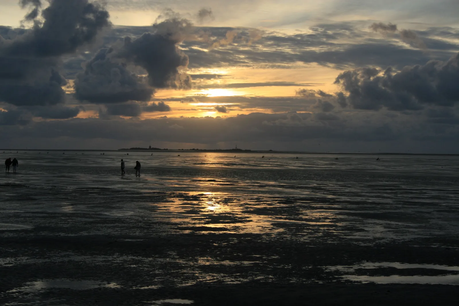 Wattwanderer bei Sonnenuntergang im Nationalpark Niedersächsisches Wattenmeer vor Cuxhaven-Duhnen, am Horizont Neuwerk
