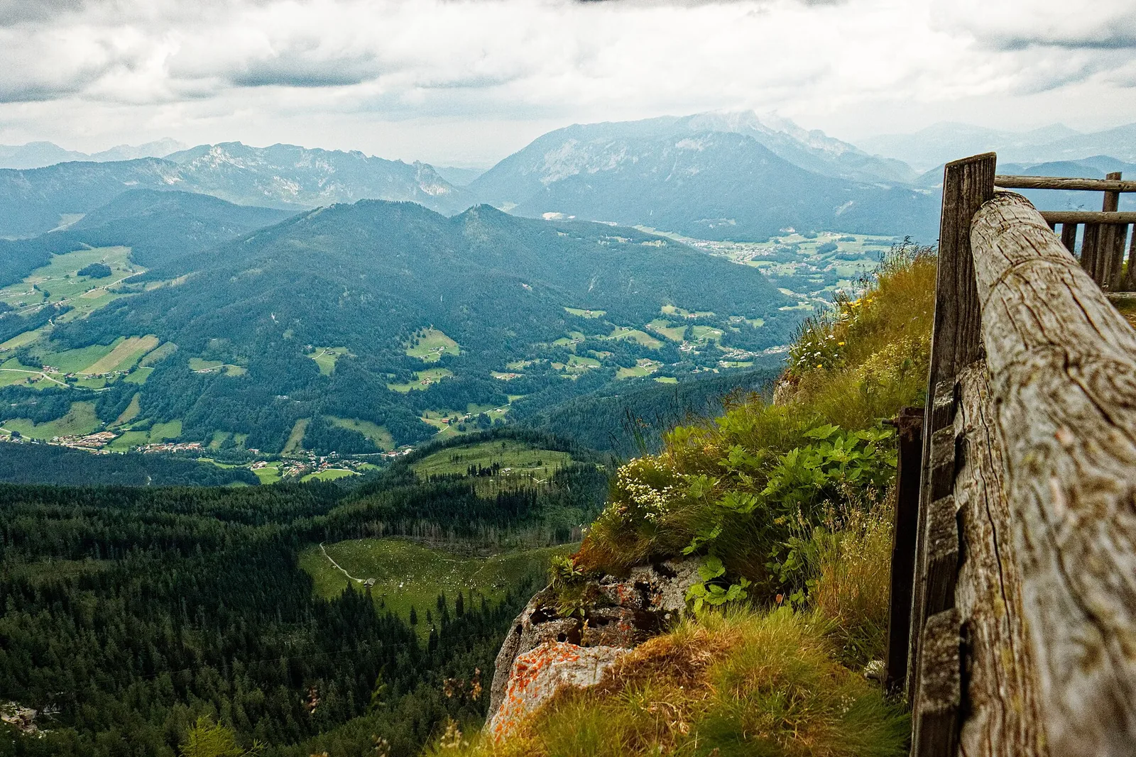 Blick vom Watzmannhaus über einen Holzzaun hinunter ins Berchtesgadener Tal und auf die umliegenden Berge