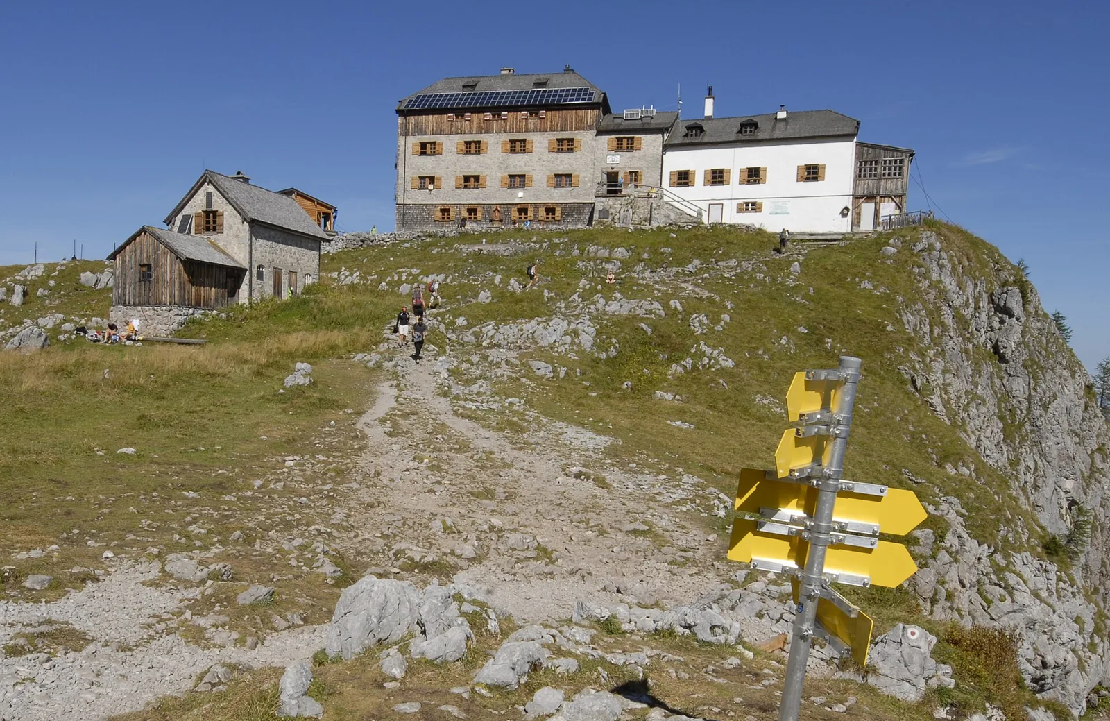 Das Watzmannhaus mit Nebengebäuden auf dem Falzköpfl, im Vordergrund gelbe Wegweiser des Nationalparks Berchtesgaden