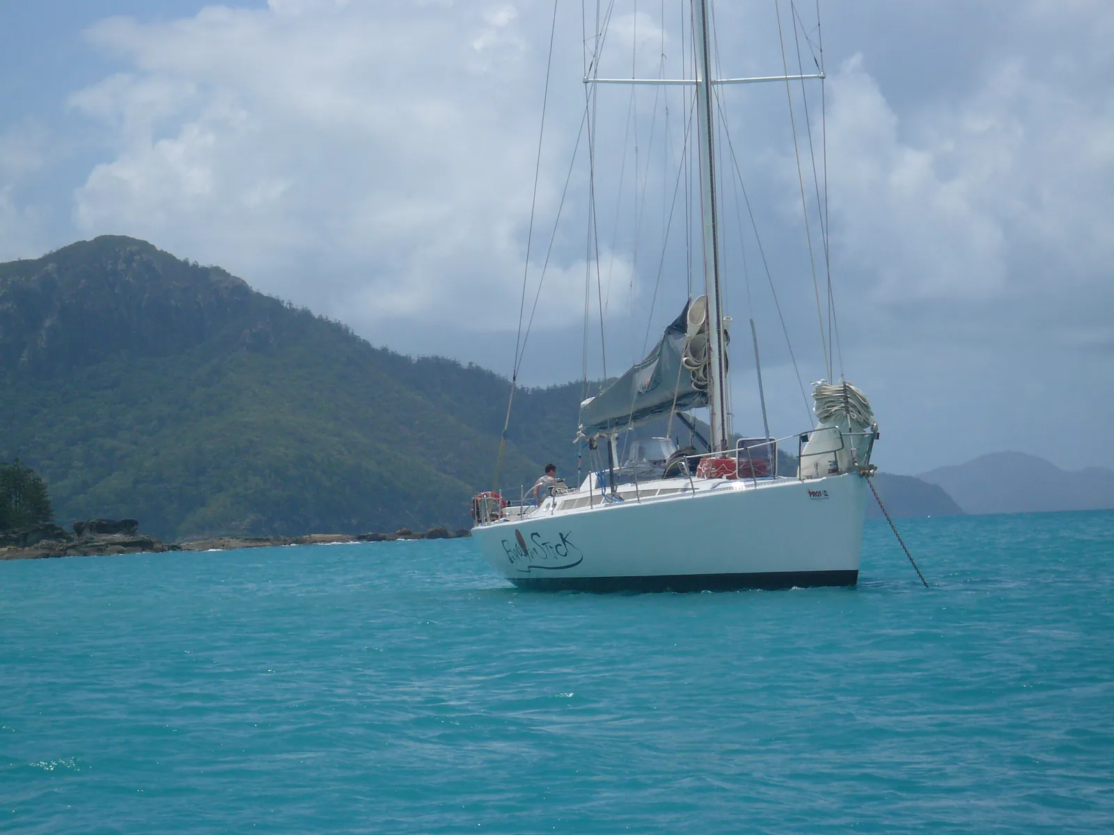 Eine Segeljacht liegt in einer Bucht der Whitsunday Islands im Great Barrier Reef, dahinter bewaldete Hügel