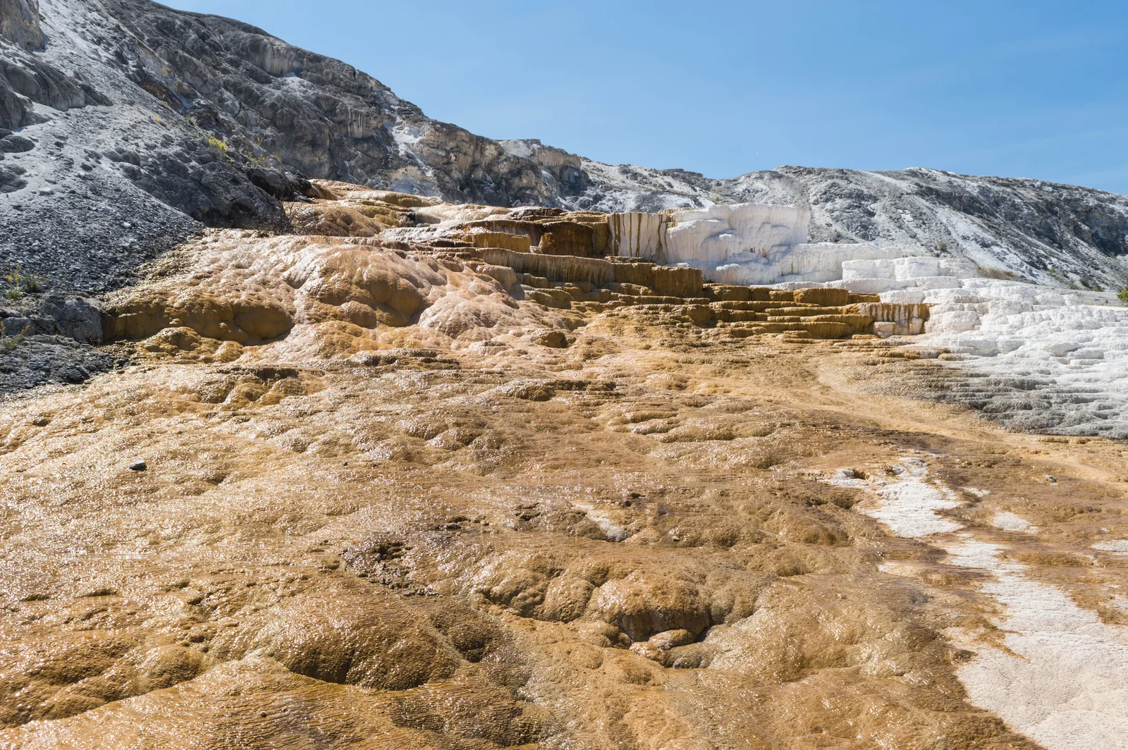 Gestufte weiße Sinterterrassen mit orangen Streifen, über die dünne Wasserfilme laufen